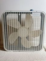 Full view of off-white box fan with grille and blades