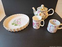 Group view of teapot, two mugs and fluted serving plate