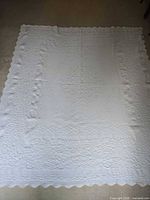 Full view of white quilt laid flat showing overall size and scalloped perimeter