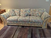 Front view of rattan sofa with three seat and three back cushions in pastel floral fabric on a rug