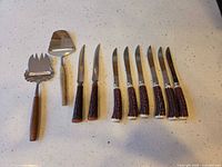 Full set laid out: eight steak knives, cheese fork, cheese plane