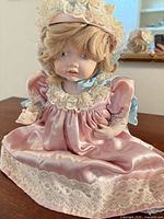 Full view of doll seated showing dress and bonnet