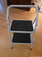 front view of unfolded stool showing two black steps and white frame