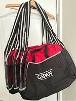 Six red and black tote bags hanging, showing C-SPAN logo side