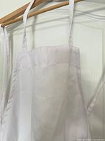 Close view of upper section of white apron on hanger