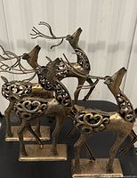 Side view of four bronze-tone metal reindeer with scrollwork bodies