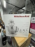Front of sealed KitchenAid Artisan stand mixer box showing product image and attachments