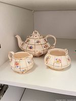 Front view of teapot, sugar bowl, and creamer on shelf