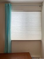 Window with beige pleated shade, aqua sheer panel and silver rod
