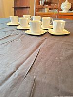 Seven white porcelain espresso cups on matching saucers displayed on table