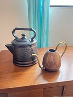 Watering can and ceramic teapot side by side on tabletop