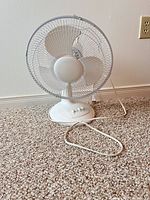 Front view of white table fan showing blades, grille, base, power cord
