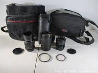Group shot of three lenses with caps, two camera bags and two filters
