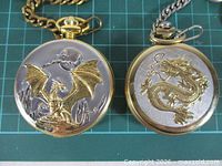 Front views of both pocket watches showing dragon relief designs and crowns