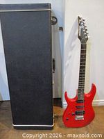 Front view of red Ibanez EX Series guitar standing beside closed black hard case