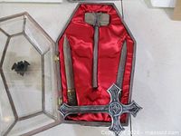 Open coffin box showing red satin lining, cross, hammer and stake