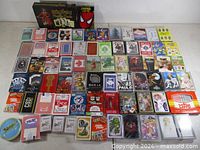 Full spread of roughly 70 playing card decks laid out on table showing variety and quantity
