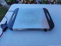 Top view of stainless steel griddle with cord attached, showing full cooking surface and handles