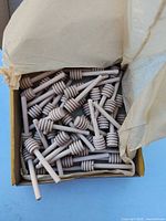 Open box showing many natural wood honey dippers