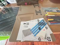 Sealed 3M privacy filter with instruction sheet, installation strips, cloth and pens visible at right
