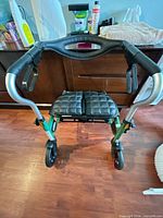 Front view of green rollator walker showing seat, wheels and hand brakes