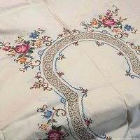 Close-up of tablecloth showing cream fabric, floral embroidery and lace insert