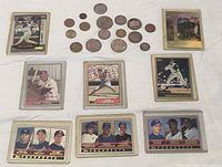 Eight baseball cards in plastic holders with sixteen mixed foreign coins displayed
