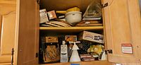 Cupboard shelf with calzone press, cannoli forms box, trivets, mixing bowl and other gadgets