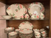 Overall view of two shelves showing majority of dishes including plates, bowls, platters and serving pieces