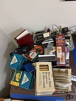 All items piled on table showing calculators, desk organizer box, calendar, tape rolls, rubber band boxes, notebook and accessories
