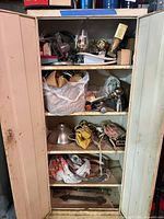 Full cabinet with shelves of assorted hardware, hoses, lamp parts, pipe wrenches visible