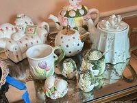 Group shot showing all four teapots, mug, shakers and egg ornament on mirrored surface
