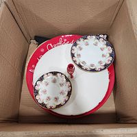 Box containing red cookie plate, white plate, two patterned saucers and red stem glass