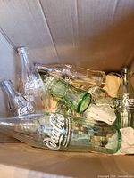 Open box containing multiple empty Coca-Cola glass bottles with embossed logos