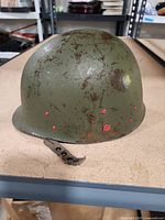 Left-front view of M1 helmet showing red plugs and chinstrap hardware