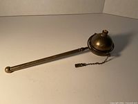 Full view of brass weighted sphere oil lamp with handle and snuffer chain