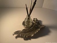 Full view of silver-plate inkstand with glass inkwell and pens for scale