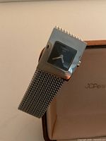 Front view of watch on display case showing black dial marked Tissot 1853 and mesh bracelet