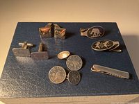 Front view of all cufflinks and tie clips on blue surface