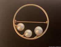 Front view of circular brooch showing three pearls in gold frame