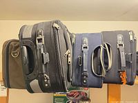 Side view of three stacked wheeled suitcases showing colors black, grey, navy and telescoping handle housings