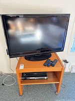 Overall view of Dynex TV on wooden stand with DVD player and remotes visible