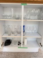 Cabinet with assorted clear and blue glassware: wine glasses, tumblers, vases, candle holder and corkscrew