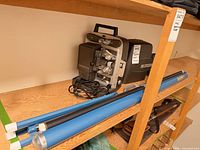 Projector, two blue roll-up screens and slide viewer case on shelf