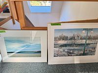 Both art pieces leaning against stair rail: framed photograph left, unframed print right
