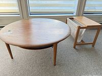 Top view of round wood coffee table beside wood magazine rack with canvas sling