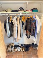 Wide closet view showing mixed outerwear on hangers, hats on shelf, footwear on floor rack