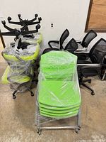 Group shot showing two wrapped green task chairs, stack of green plastic chairs, and row of black mesh chairs