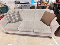 Front view of beige woven fabric three-seat sofa with three throw pillows