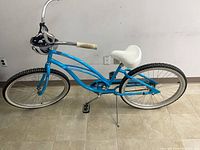 Right-side view of blue step-through cruiser bike with helmet on handlebars showing frame, wheels, saddle, and kickstand